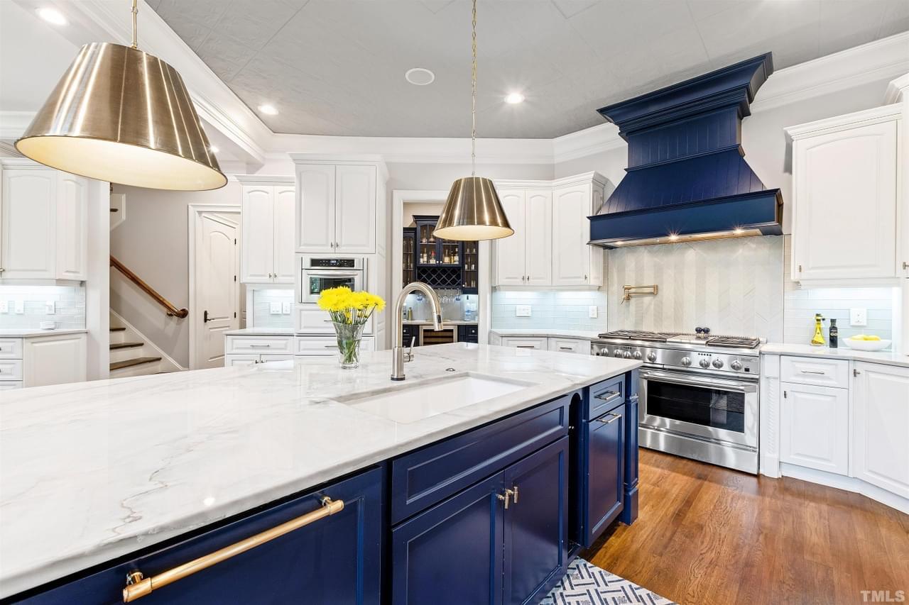 A bright kitchen with bold blue cabinetry and matching stove hood, white countertops, and gold accents